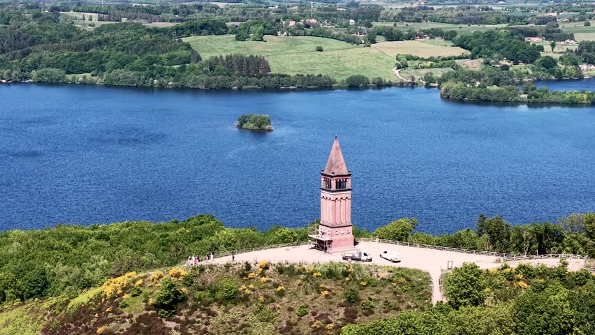 Aerial footage of the Himmelbjerget tower rising above the landscape, with a blue lake and green woodlands in the background.
