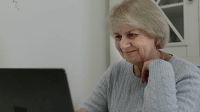 Mature female retiree comfortably working on laptop, enjoying digital communication while wearing blue sweater and smiling warmly against clean white background - Powered by Shutterstock - Get 15% off with code: PIKWIZARD15