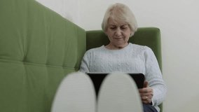 Relaxed senior woman using digital tablet while sitting comfortably on green sofa, experiencing technology with calm enjoyment and peaceful connection at home - Powered by Shutterstock - Get 15% off with code: PIKWIZARD15