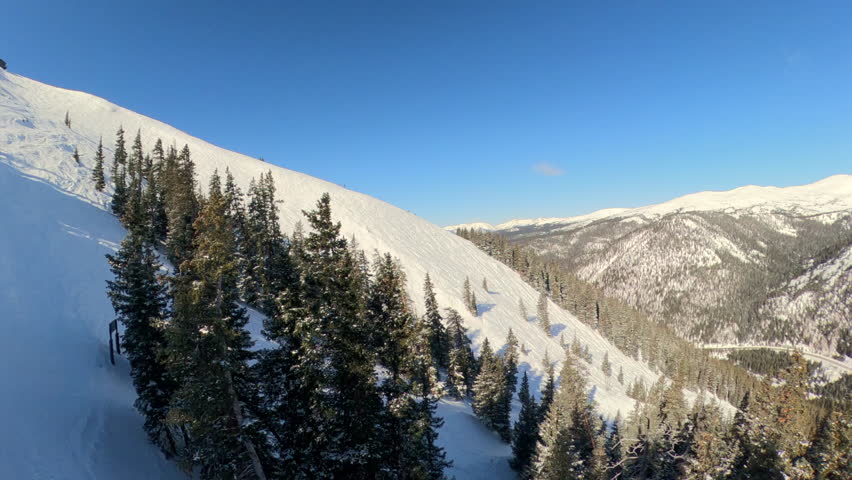 While riding a chairlift, the camera smoothly pans from the rugged mountainside to the lift ahead, revealing a sweeping view of the alpine landscape.