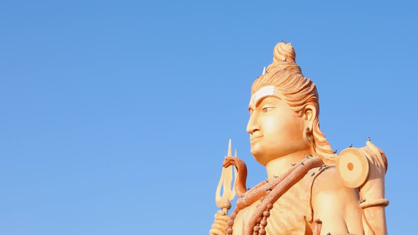 divine sculpture of lord shiva holding trident and damru with bright blue sky background