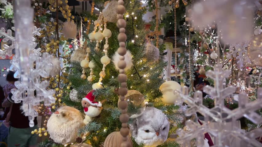 Colorful glittering ornaments hang from a Christmas tree against a backdrop of festive lights in a store. Space for text.