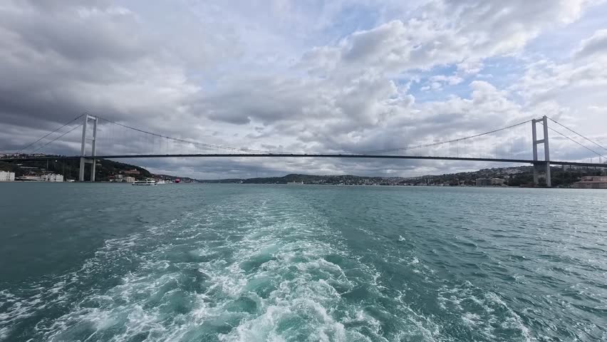Bosphorus Bridge spanning strait in Istanbul, Turkey viewed from ferry with dramatic clouds and turquoise water