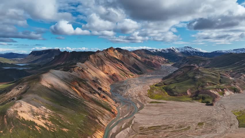 A drone ascends over Landmannalaugar, revealing colorful rhyolite mountains and braided glacial rivers under bright summer skies.