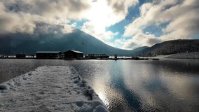 Clear mountain lake stretches from a snow edged dock toward rugged snowy peaks wrapped in drifting clouds, under bright blue sky and soft winter light in Alberta, Canada. - Powered by Shutterstock - Get 15% off with code: PIKWIZARD15