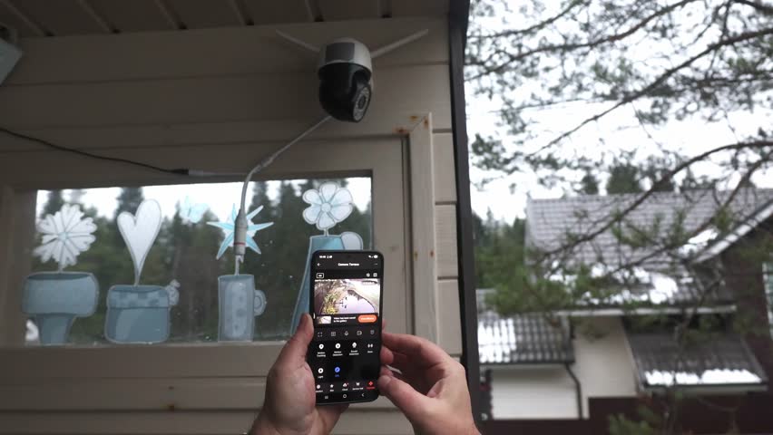 Hands holding hold smartphone that controls outdoor security camera. control home using smart home mobile app. High quality 4k footage