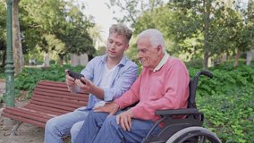 Grandson and senior man in a wheelchair looking at a smartphone together while sitting in the park - Powered by Shutterstock - Get 15% off with code: PIKWIZARD15