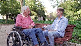 Grandson reading a book to his elderly grandfather in a wheelchair in the park - Powered by Shutterstock - Get 15% off with code: PIKWIZARD15