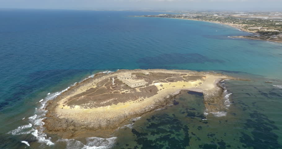 Aerial view of Isola delle Correnti, a small rocky island near the coast. In background is the Sicilian coastline, located near Portopalo in the province of Syracuse, Sicily, Italy. Sunny summer day.