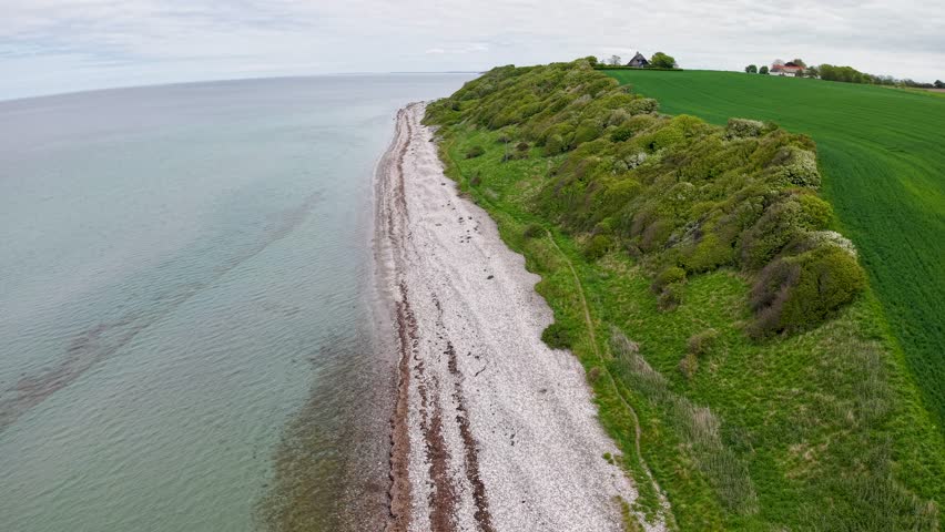 Aerial drone footage of dramatic white cliffs and turquoise waters along a green coastline in Denmark.