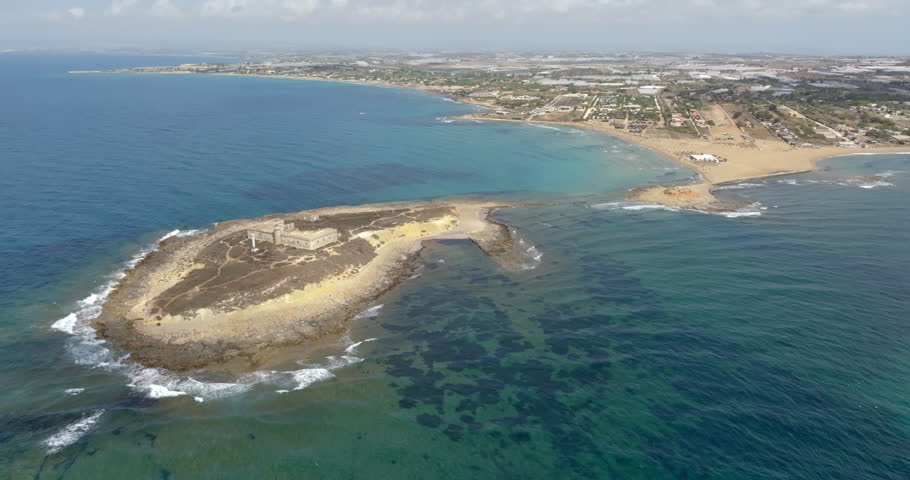 Aerial view of Isola delle Correnti, a small rocky island near the coast. In background is the Sicilian coastline, located near Portopalo in the province of Syracuse, Sicily, Italy. Sunny summer day.