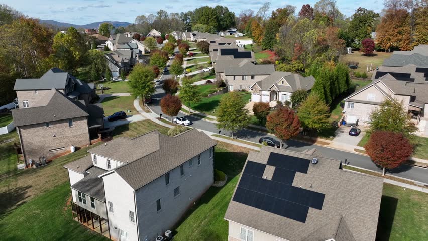 Well-kept luxury housing area of American neighborhood at sunlight. Solar panel units installed on roof of homes. Cars and well-maintained garden in quiet suburb. Sunny day in autumn season.