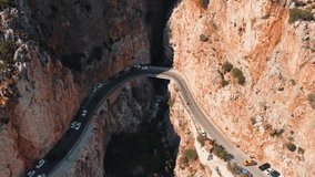 Aerial drone view showing winding canyon road and tunnel route cutting through rugged Saklikent Gorge in Mugla, capturing steep rock walls, moving traffic, narrow passage, and warm summer light - Powered by Shutterstock - Get 15% off with code: PIKWIZARD15