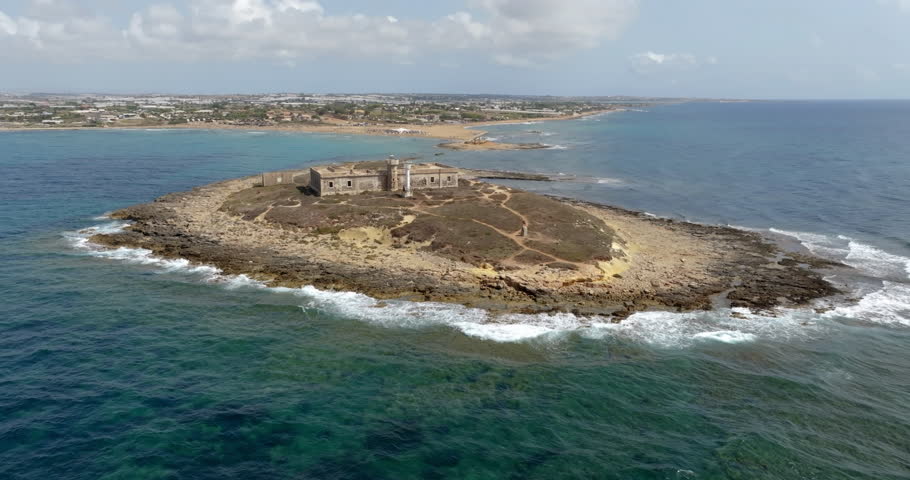 Aerial view of Isola delle Correnti, located near Portopalo in the province of Syracuse, Sicily, Italy. There is an old, abandoned lighthouse. The island is surrounded by the Mediterranean Sea.