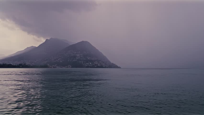 Lugano, Switzerland – September 24, 2022: Rainy view of Monte Brè fading into fog above the calm waters of Lake Lugano.