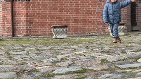 low angle view of adult legs in grey jeans and black boots walking hand in hand with child in blue wet pants and beige shoes on red brick street wet cobblestone rainy day urban scene no faces visible - Powered by Shutterstock - Get 15% off with code: PIKWIZARD15