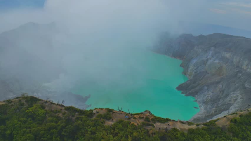 A misty aerial view of the turquoise lake inside Kawah Ijen crater, surrounded by rugged volcanic rock in East Java, Indonesia