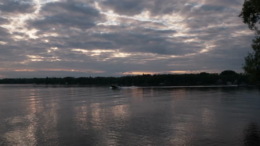 A calm lake under heavy clouds reflects soft fading light as a small boat moves gently across the water