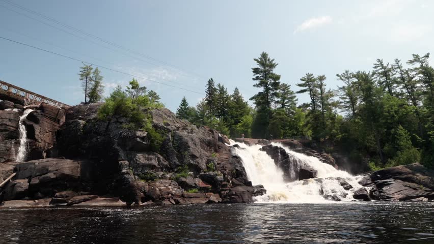 A static shot of a powerful waterfall on granite rock with evergreen pine trees on top on a sunny summer day in northern Canada, High Falls Park