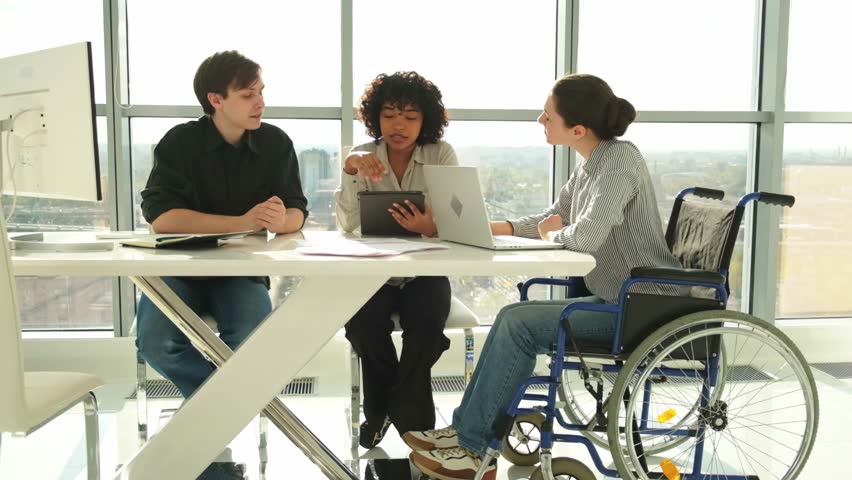 Teamwork brainstorm. Diverse multiracial colleagues woman in chair for people with disability working together. Group of people sitting in creative office discussing business. Young professional team - Powered by Shutterstock - Get 15% off with code: PIKWIZARD15