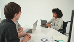 Teamwork brainstorm. Diverse multiracial colleagues woman in chair for people with disability working together. Group of people sitting in creative office discussing business. Young professional team - Powered by Shutterstock - Get 15% off with code: PIKWIZARD15