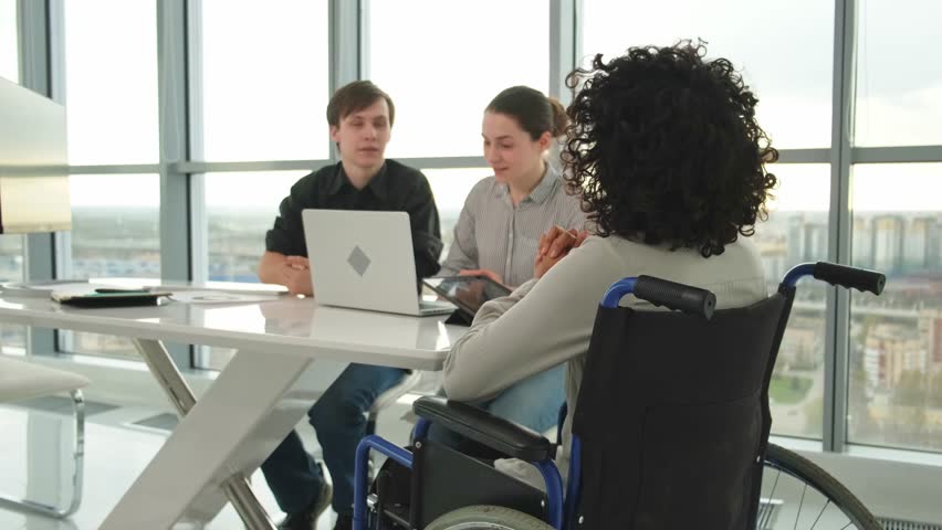 Teamwork brainstorm. Diverse multiracial colleagues woman in chair for people with disability working together. Group of people sitting in creative office discussing business. Young professional team - Powered by Shutterstock - Get 15% off with code: PIKWIZARD15