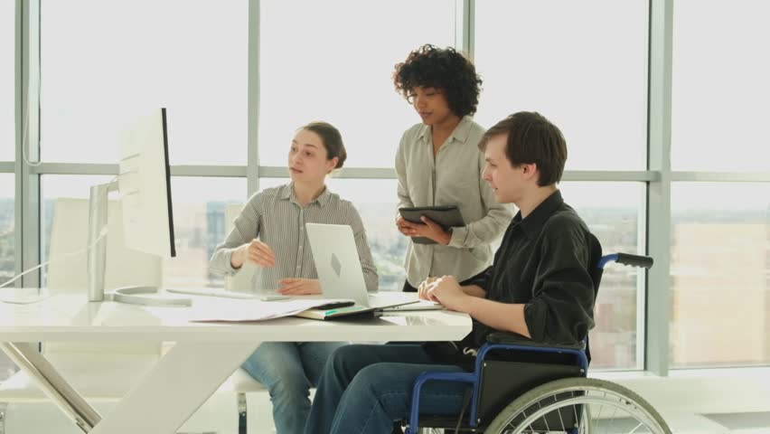 Teamwork brainstorm. Diverse multiracial colleagues man in chair for people with disability working together. Group of people sitting in creative office discussing business. Young professional team - Powered by Shutterstock - Get 15% off with code: PIKWIZARD15