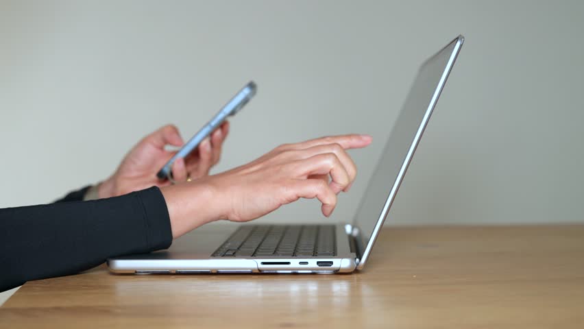 Businesswoman using laptop and smartphone, remote work concept. Modern office desk with technology for online work, productivity and communication in professional digital workplace.
