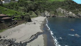 Aerial view of a bright coastline featuring powerful ocean waves, dark cliffs, and a soft sandy beach framed by fresh spring greenery - Powered by Shutterstock - Get 15% off with code: PIKWIZARD15