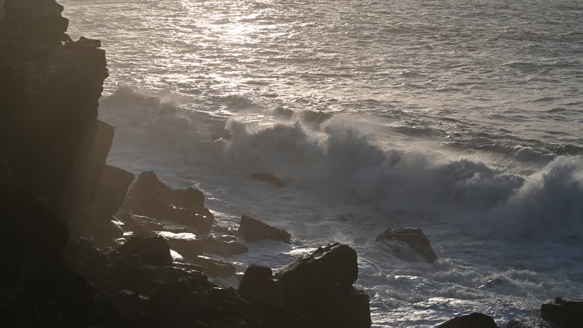 Strong Atlantic waves roll against dark coastal rocks, highlighting the power of the sea and the rugged textures of the natural shoreline in Peniche Portugal during late afternoon.