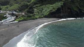 A wide 4K drone shot capturing the dramatic black sand shoreline of beach dos Mosteiros, with soft waves rolling in and the volcanic landscape shining under bright daytime light. - Powered by Shutterstock - Get 15% off with code: PIKWIZARD15