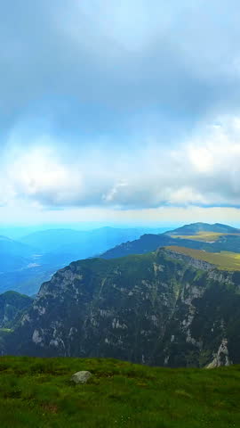 Steep cliffs with grassy plateau and thick clouds casting shadows. Rugged and vivid romanian mountain terrain.