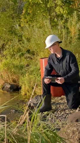 Scientist crouches down inspecting water sample from stream during fieldwork, vertical