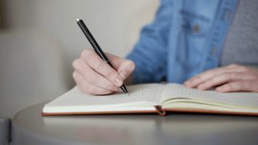 Closeup of a woman's hand writing in a notebook with a pen. The young female student is studying, working, journaling, writing while sitting at adesk with a blurred background. Cropped take notes - Powered by Shutterstock - Get 15% off with code: PIKWIZARD15