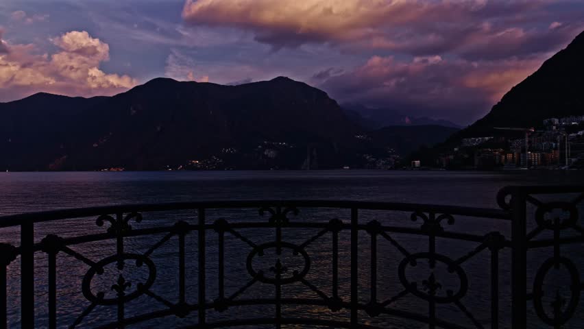 Paradiso, Switzerland – October 5, 2022: View across Lake Lugano toward Monte San Salvatore and Monte Caprino, framed by decorative metal railing in the foreground.
