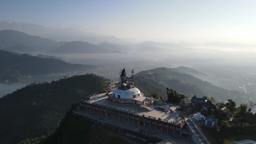 Drone aerial view of the Shiva statue in Pumdibhumdi, Pokhara, Nepal — hilltop monument overlooking Phewa Lake and the Annapurna Himalayas.