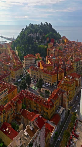  Aerial view of bustling beachfront promenade on sunny day. Beautiful panorama in Nice, France. Palm trees, old houses in old town azure sea and green hills. Summer in French Riviera