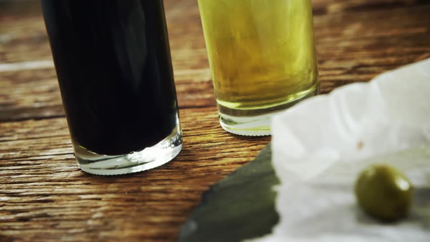Gold confetti falling, camera panning right, zooming, olives rolling toward bread, showing pile. Olive, parchment, rustic, tabletop, slate, mediterranean, gourmet