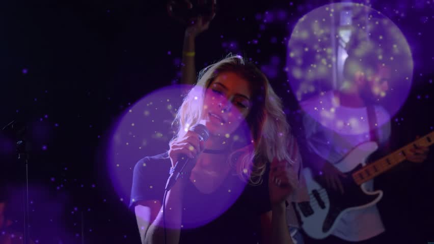 Lead vocalist lowering head to mic, causing hair flips while band singing, purple bokeh over stage. Singer, livemusic, lighting, movement, energy, ensemble, concert