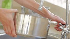 Left hand turning faucet, water flowing into stainless steel pot while right hand rinsing to clean. Cookware, sink, tap, kitchen, closeup, glossy, metal - Powered by Shutterstock - Get 15% off with code: PIKWIZARD15