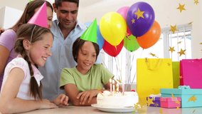 Parents encouraging kids blowing birthday cake candles, confetti rising and balloons drifting. Family, celebration, presents, hats, joy, daylight, home - Powered by Shutterstock - Get 15% off with code: PIKWIZARD15