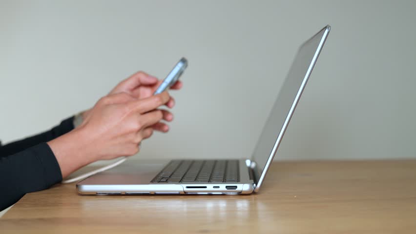 Businesswoman using laptop and smartphone, remote work concept. Modern office desk with technology for online work, productivity and communication in professional digital workplace.

