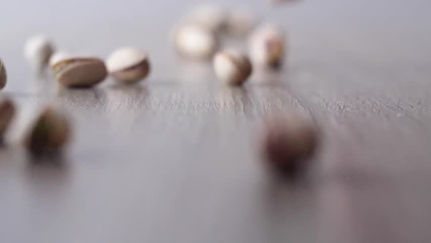 Slow Motion: Pistachio Nuts Falling and Bouncing on Wooden Table Surface - Action shot of hard shell nuts hitting a wooden surface and jumping up