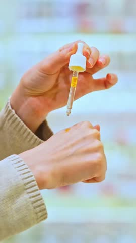 Vertical video: Woman testing serum texture on her hand before purchase in a beauty store, making an informed choice while selecting a cosmetic product for skincare.