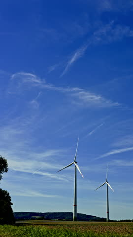 Tall white windmills against a blue sky. Wind turbines spinning and producing alternative energy. Windmills in a field somewhere in the countryside in Europe.