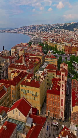  Aerial view of bustling beachfront promenade on sunny day. Beautiful panorama in Nice, France. Palm trees, old houses in old town azure sea and green hills. Summer in French Riviera