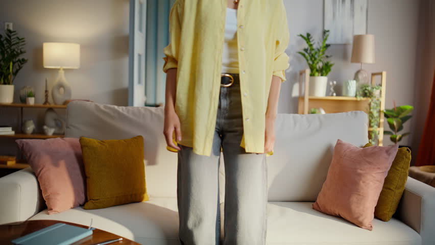 Tired woman resting cozy couch wearing yellow shirt. Tranquil young lady sitting comfortable home sofa enjoying light apartment interior. Curly brunette chilling relaxing in calm domestic atmosphere.