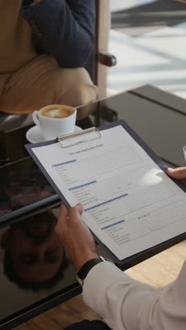 Vertical closeup shot of car dealer holding clipboard with document and discussing terms of sale with man choosing new car