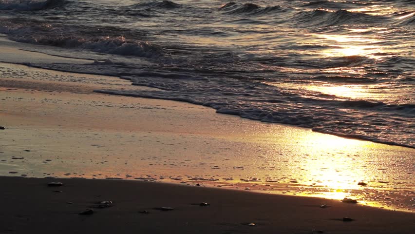 Close-up wave crashes onto the sand on a beach at golden sunset. Wavy Baltic sea. Normal speed with sound.