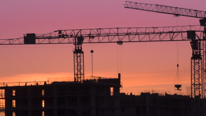 Building a House at Sunset. Time-Lapse. Three tower cranes tower over a residential complex under construction. Intense work in progress against the background of the evening sky